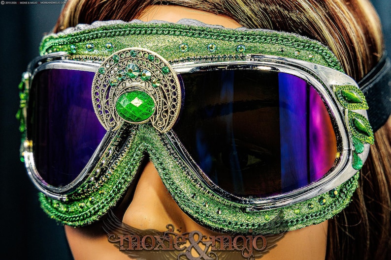 Pu&ograve; includere: Occhiali protettivi verdi con montatura in metallo argentato e lenti color viola scuro. La montatura &egrave; decorata con glitter verdi, piccoli strass verdi e un emblema centrale in filigrana color oro con una grande pietra verde ovale.