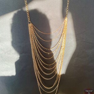 May include: A gold layered chain necklace with small round beads. The necklace is on a dark gray background.