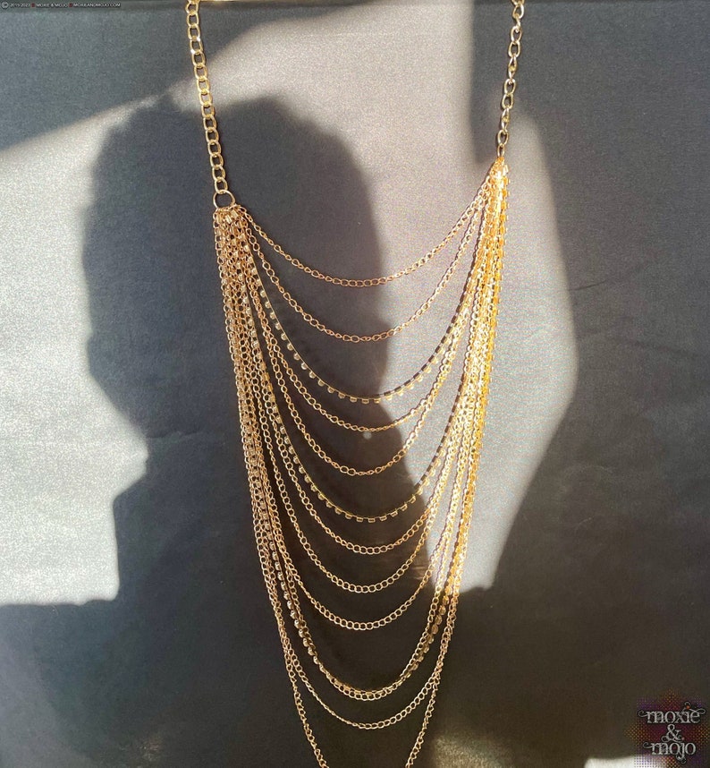 May include: A gold layered chain necklace with small round beads. The necklace is on a dark gray background.