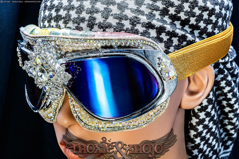 Puede incluir: Gafas protectoras con lentes azul oscuro y una montura decorada con cristales transparentes y pedrer&iacute;a. Incluyen una cinta el&aacute;stica dorada y se llevan sobre un pa&ntilde;uelo con estampado en blanco y negro que muestra el texto moxie & mojo.