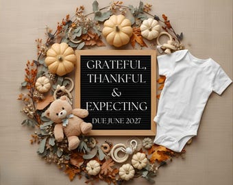May include: A white baby bodysuit next to a square letter board with the text GRATEFUL, THANKFUL & EXPECTING DUE JUNE 2027, surrounded by a wreath of autumn leaves, small cream-colored pumpkins, wooden baby rings, and a plush tan teddy bear.