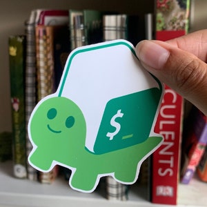 May include: A die-cut vinyl sticker featuring a light green cartoon turtle with a smiling face. The turtle carries a white and dark green laptop shell on its back, which displays a white dollar sign and an underscore symbol on the screen.