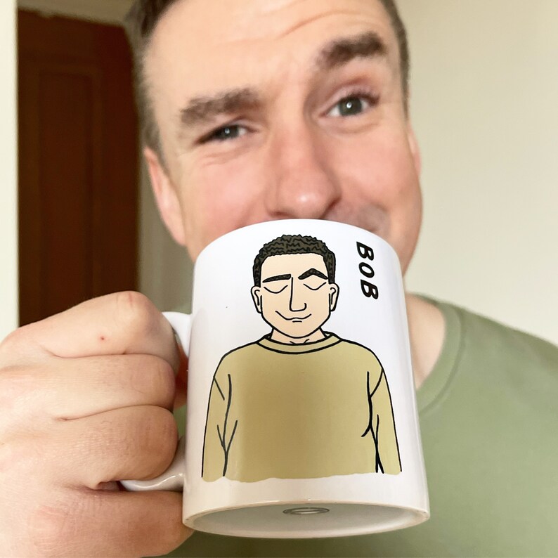 May include: White ceramic mug with a cartoon illustration of a person with brown hair and a tan sweater. The text "BOB" is printed on the mug.