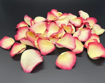May include: A pile of rose petals with a cream base and a pink edge. The petals are scattered on a black surface.