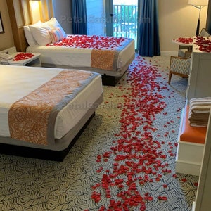 K&ouml;nnte beinhalten: Zwei Einzelbetten mit wei&szlig;en Bettw&auml;sche und roten Rosenbl&auml;ttern, die auf dem Bett und dem Boden verstreut sind. Das Zimmer hat einen gemusterten Teppich und einen Blick auf einen Balkon.