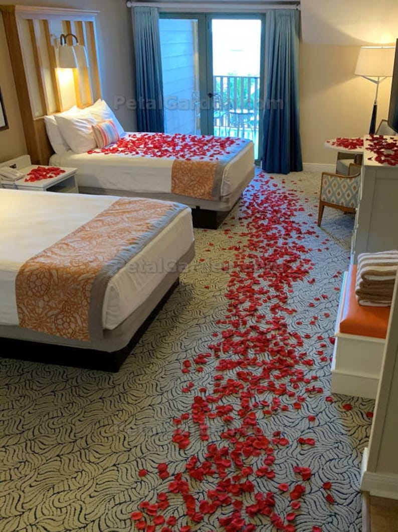 K&ouml;nnte beinhalten: Zwei Einzelbetten mit wei&szlig;en Bettw&auml;sche und roten Rosenbl&auml;ttern, die auf dem Bett und dem Boden verstreut sind. Das Zimmer hat einen gemusterten Teppich und einen Blick auf einen Balkon.