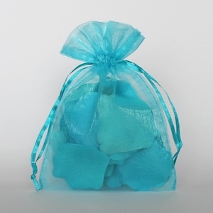 Puede incluir: Una bolsa de organza azul turquesa llena de pétalos de rosa de seda azul turquesa. La bolsa tiene un cierre de cordón.