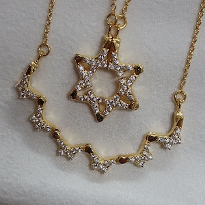 May include: A gold necklace featuring a Star of David pendant and a matching chain with a delicate design. The necklace is made of gold and has a sparkly finish.