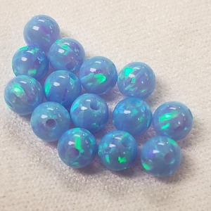 May include: A collection of 12 light blue opal beads with iridescent green and purple flecks. The beads are round and have a smooth, polished finish.