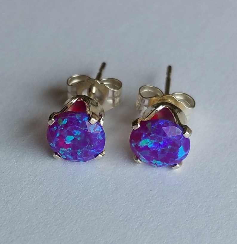 May include: A pair of silver stud earrings with round purple opal stones. The stones have a sparkly, iridescent finish.