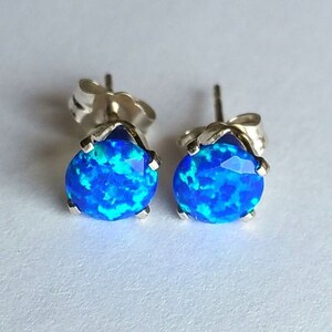 May include: A pair of silver stud earrings featuring blue opal gemstones. The opals have a blue and green iridescent shimmer.