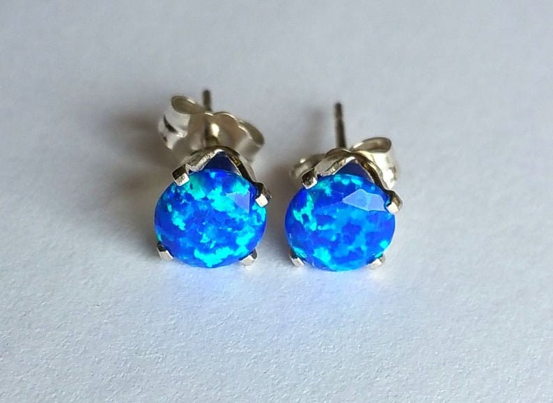 May include: A pair of silver stud earrings featuring blue opal gemstones. The opals have a blue and green iridescent shimmer.