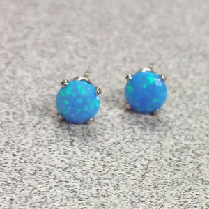 May include: A pair of silver stud earrings with blue opal stones. The stones have a light blue colour with green and white flecks.