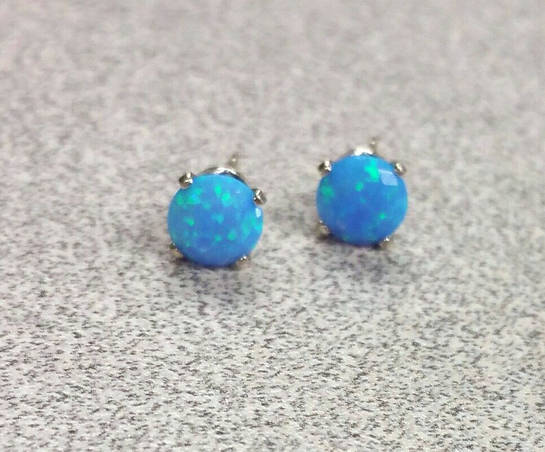 May include: A pair of silver stud earrings with blue opal stones. The stones have a light blue colour with green and white flecks.