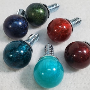 May include: Six decorative screw-on knobs with metallic silver screws. The knobs are round and have a shiny, iridescent finish. The colors of the knobs are teal, red, blue, green, and two shades of burgundy.
