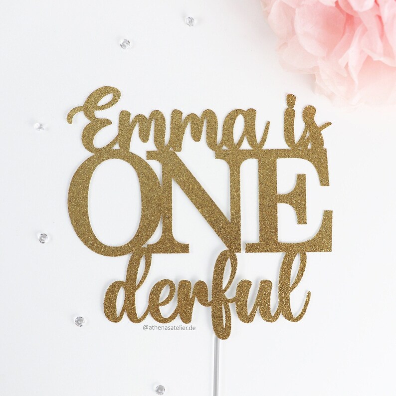 May include: Gold glitter cake topper with the text "Emma is one derful" and the Instagram handle "@athenasatelier.de".