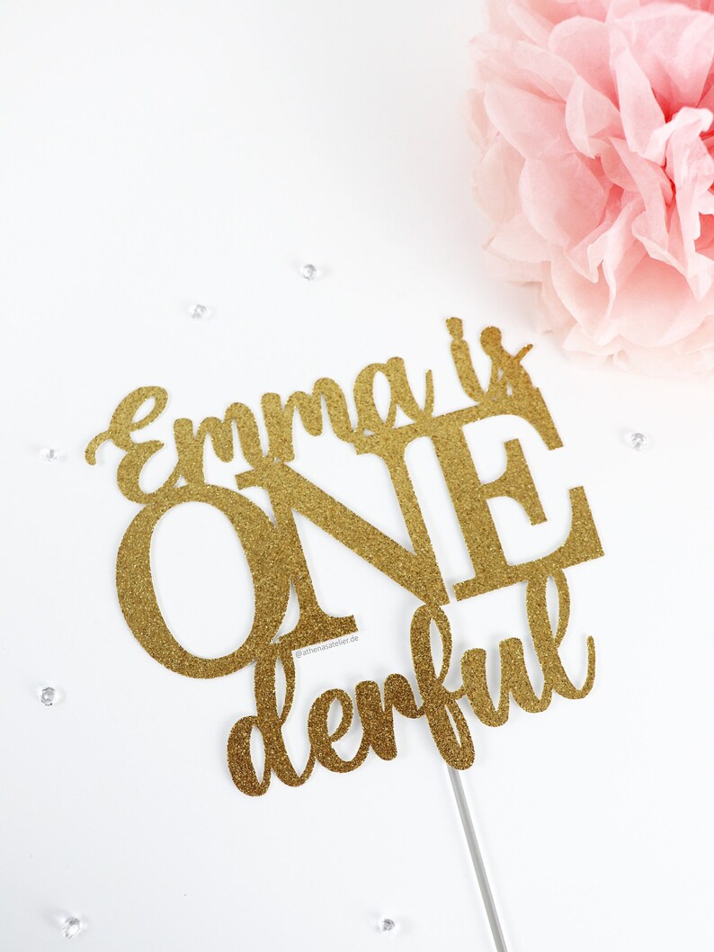 May include: Gold glitter cake topper with the text "Emma is One derful".