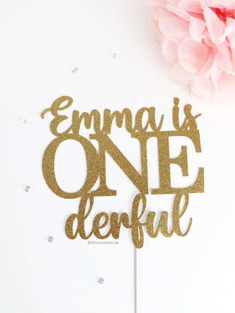 May include: Gold glitter cake topper with the text "Emma is ONEderful" and the social media handle "@athenasatelier.de".