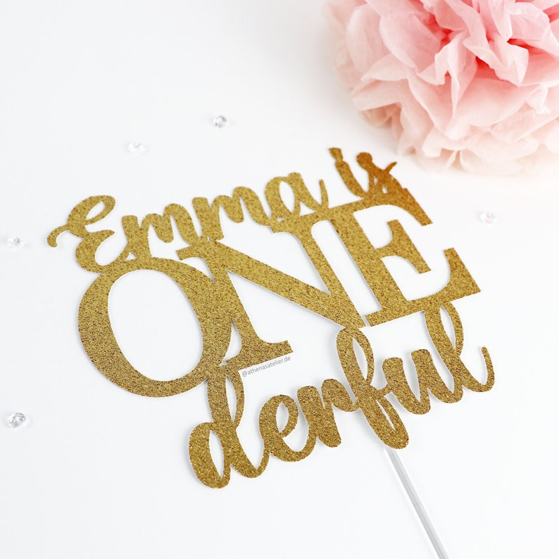 May include: Gold glitter cake topper with the text "Emma is One derful".
