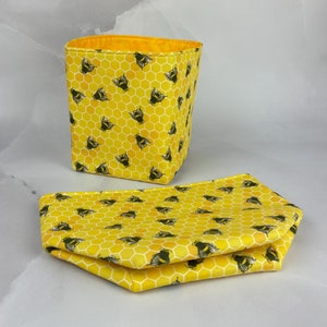 May include: A yellow fabric storage bin with a honeycomb pattern and bumblebees. The bin is sitting on a yellow fabric mat with the same pattern.