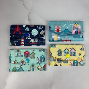 May include: Four small fabric purses with a beach hut theme. The purses are in blue, yellow, green and light blue with different patterns. Each purse has a button closure.