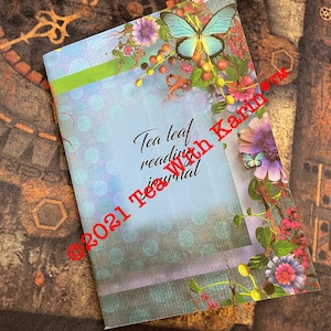 Może przedstawiać: Niebieski i zielony dziennik z motywem motyla i kwiatów. Tekst na okładce brzmi "Tea leaf reading journal" i "©2021 Tea With Karma".