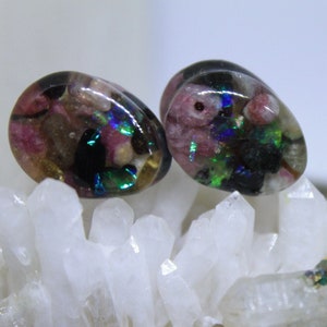 May include: Pair of teardrop-shaped glass plugs with pink, green, and black inclusions. The plugs are displayed on a bed of white quartz crystals.