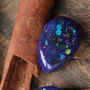 May include: Two blue resin teardrop-shaped earrings with iridescent glitter embedded in the resin.