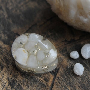 May include: A white quartz crystal with gold flecks embedded in clear resin. The crystal is shaped like a heart and is surrounded by smaller white quartz crystals.