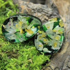 May include: Two green resin earrings with white flowers and gold accents pressed inside. The earrings are oval shaped and have a glossy finish.