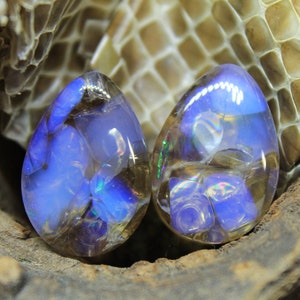May include: Two iridescent blue and brown teardrop-shaped glass beads with a swirling pattern.