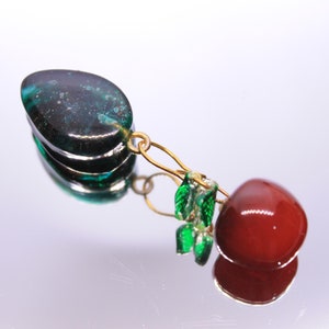 May include: A green and black glass teardrop pendant with a gold chain and green glass beads hanging from it. A red glass bead is attached to the bottom of the chain.