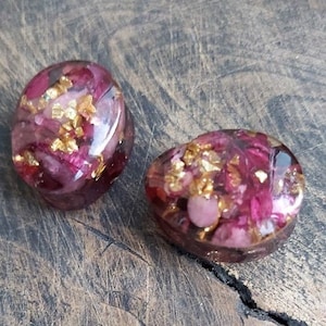 May include: Two round resin cabochons with pink and gold flecks. The cabochons are translucent and have a glossy finish.
