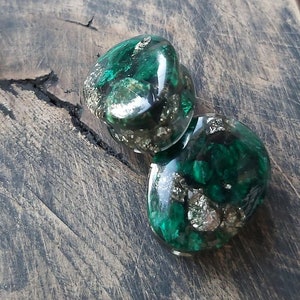 May include: Two green and gold resin heart-shaped earrings with flecks of gold and green glitter.