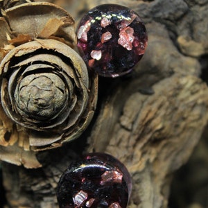 May include: Two round glass plugs with a dark purple base and embedded pink and gold glitter.