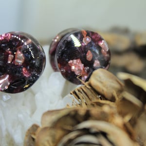 May include: Pair of round, black and purple glass ear gauges with pink and gold glitter embedded inside.