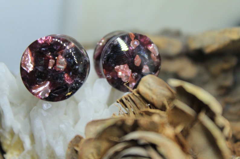 May include: Pair of round, black and purple glass ear gauges with pink and gold glitter embedded inside.