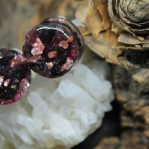 May include: Two round, dark purple glass plugs with embedded iridescent pink and gold glitter.