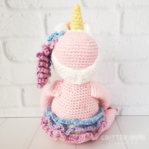 crocheted sloth in a unicorn costume facing back on a white background