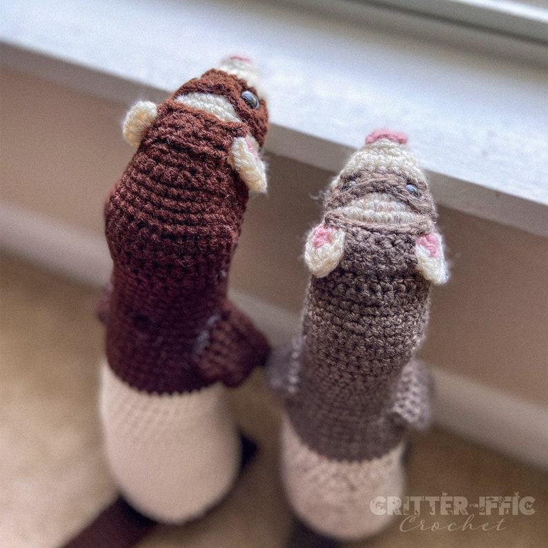 two crocheted ferrets looking out a window