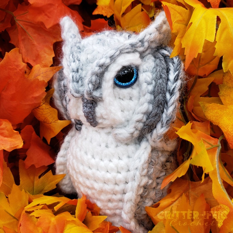 realistic crocheted white and grey owl sitting in orange leaves