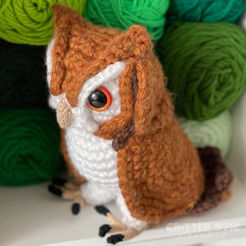 realistic crocheted screech owl sitting on a white shelf in front of green yarn