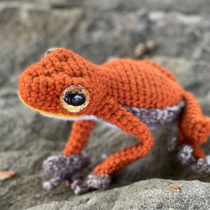 crocheted orange vampire frog version of red eyed tree frog sitting on rocks looking left