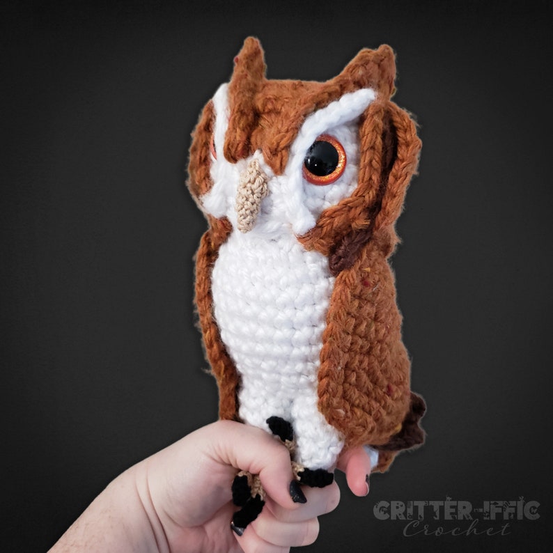 realistic crocheted screech owl sitting on a hand in front of a black background