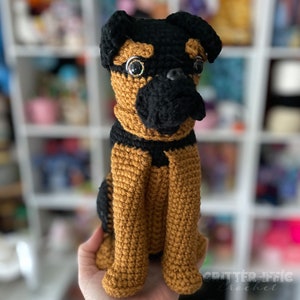 Crocheted brussels griffon dog sitting on a hand in front of a bright background