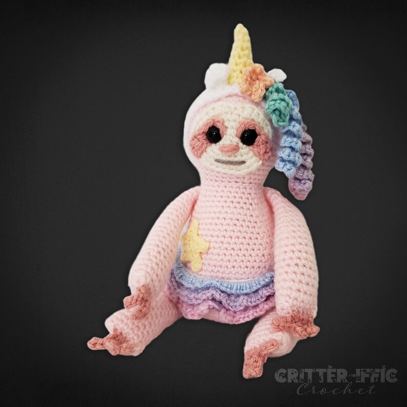 front view of crocheted pink sloth in unicorn costume on a black background