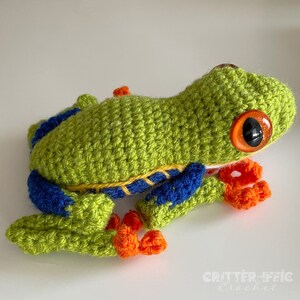 crocheted red eyed tree frog sitting on a white table looking right