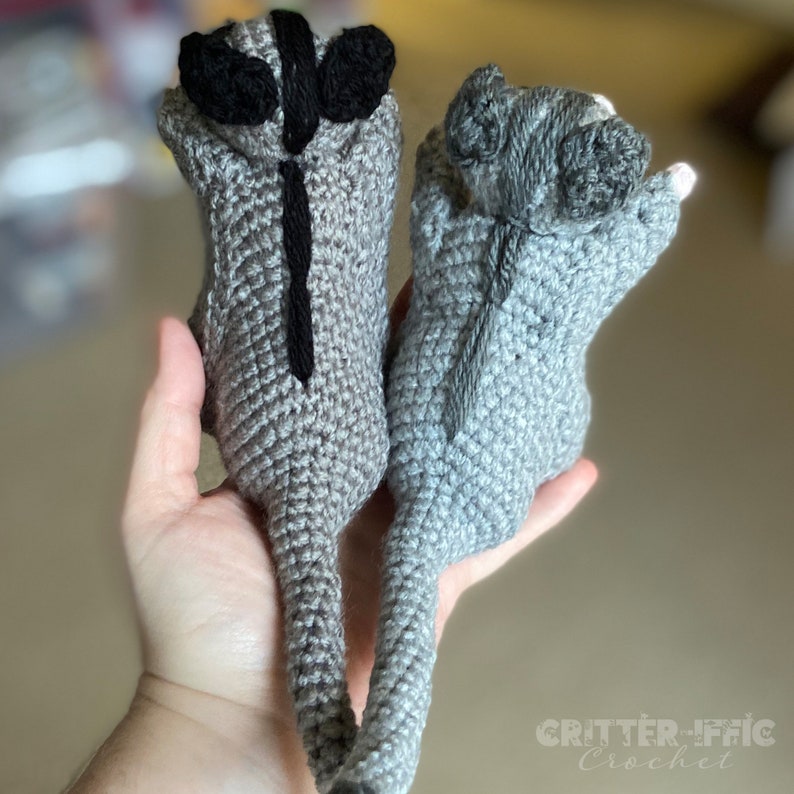 two crocheted sugar gliders showing their back to the camera to see stripe detail while held by a hand with a blurred background