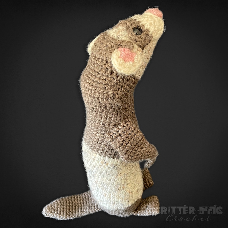 crocheted ferret looking up and to the right on a black background