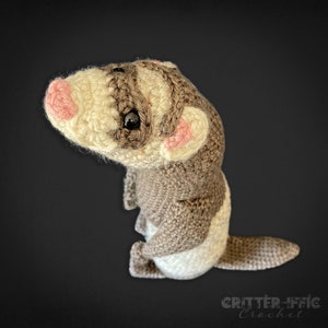 crocheted ferret on a black background looking to the left from a top angle